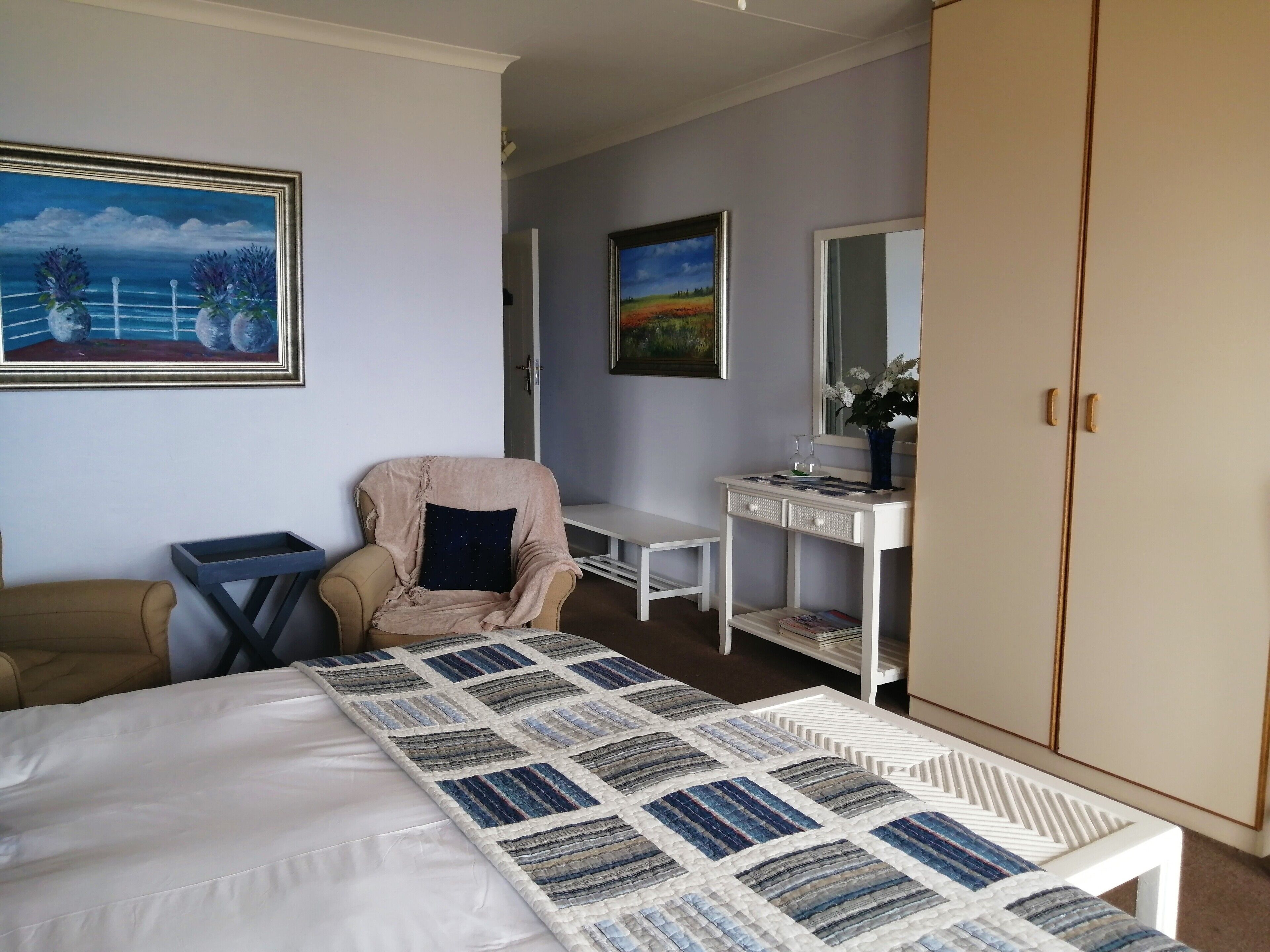 A bedroom with a bed, a chair, a desk, a wardrobe, and two paintings on the wall.