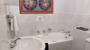 A bathroom with a sink, bathtub, and toilet. There is a framed floral artwork above the sink and a sign with water restrictions.