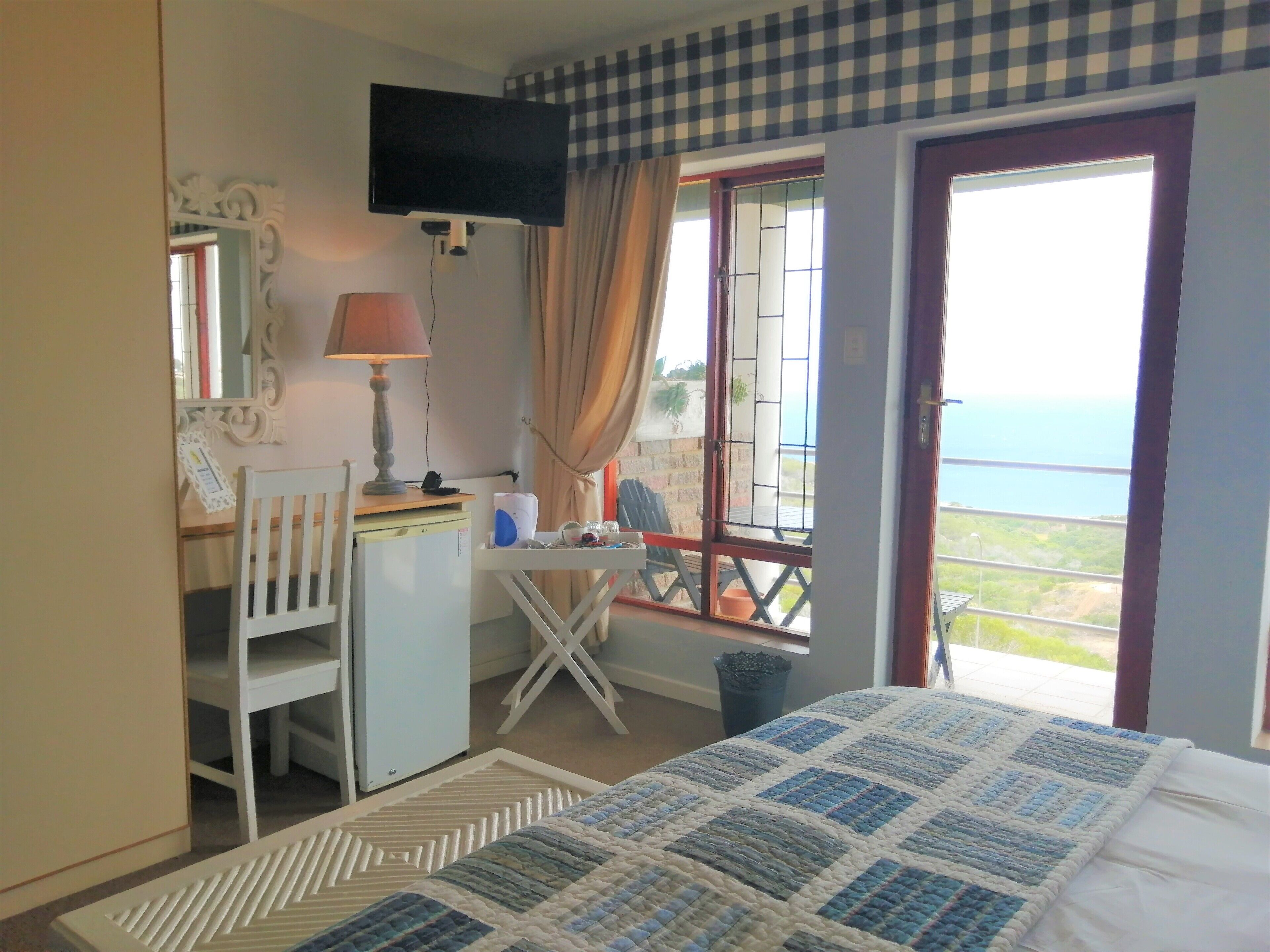 A bedroom with a bed, a desk, a chair, a television, and a window with a view of the sea.