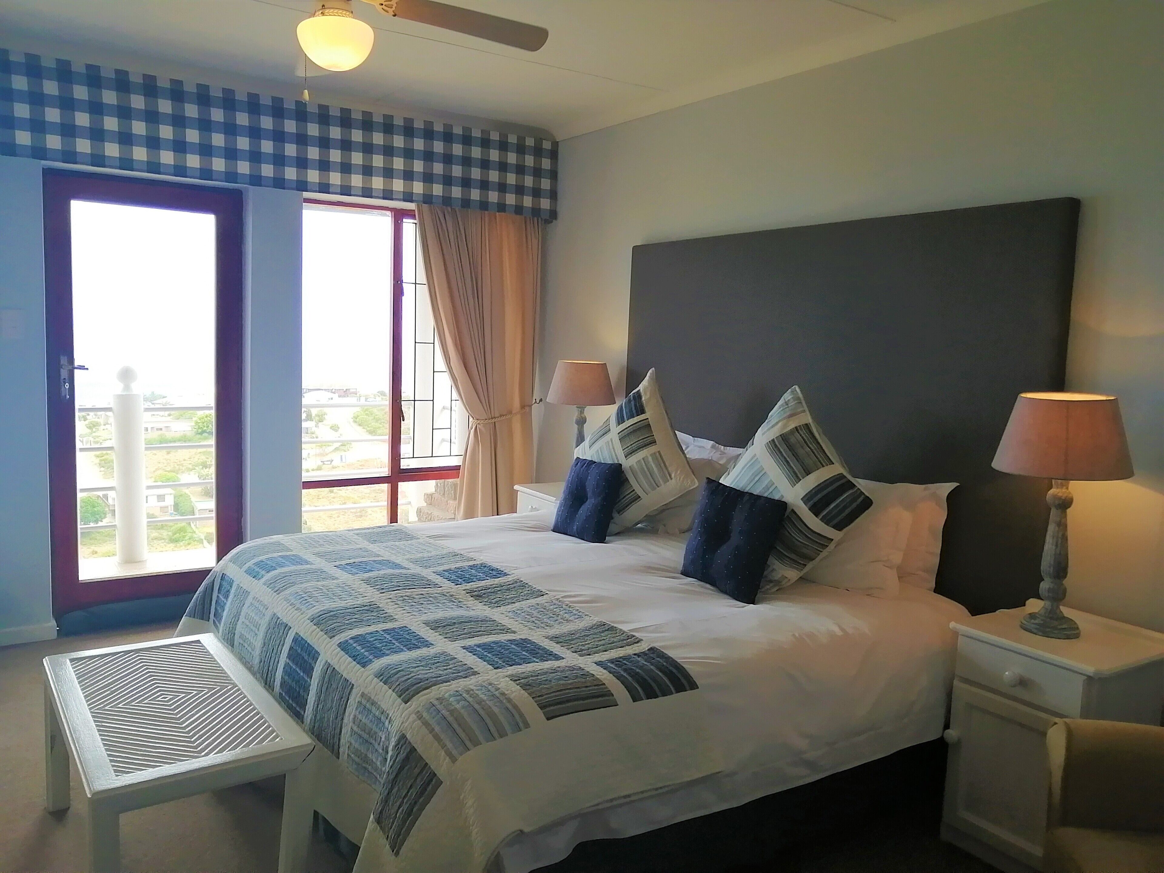 A bedroom with a large bed, two bedside tables with lamps, a window with curtains, and a view of the outside.