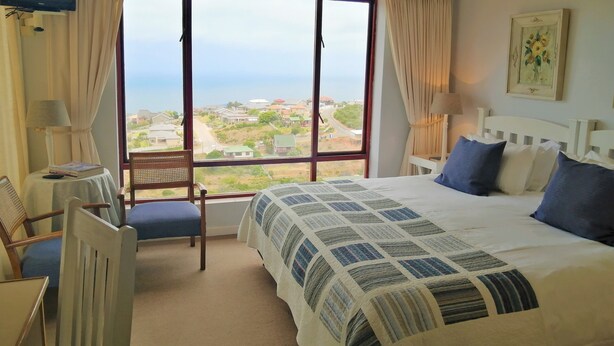 Habitación de hotel con un ventanal grande, una cama con colcha, una silla y una lámpara.