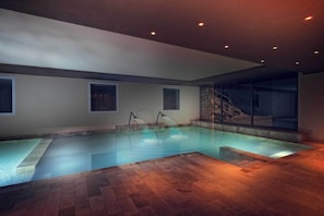 A swimming pool with a wooden deck, built-in lighting, and a stone wall.