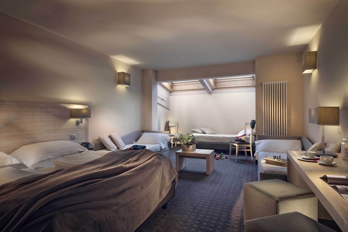 A modern hotel room with a large bed, a smaller bed, a desk, and a seating area.