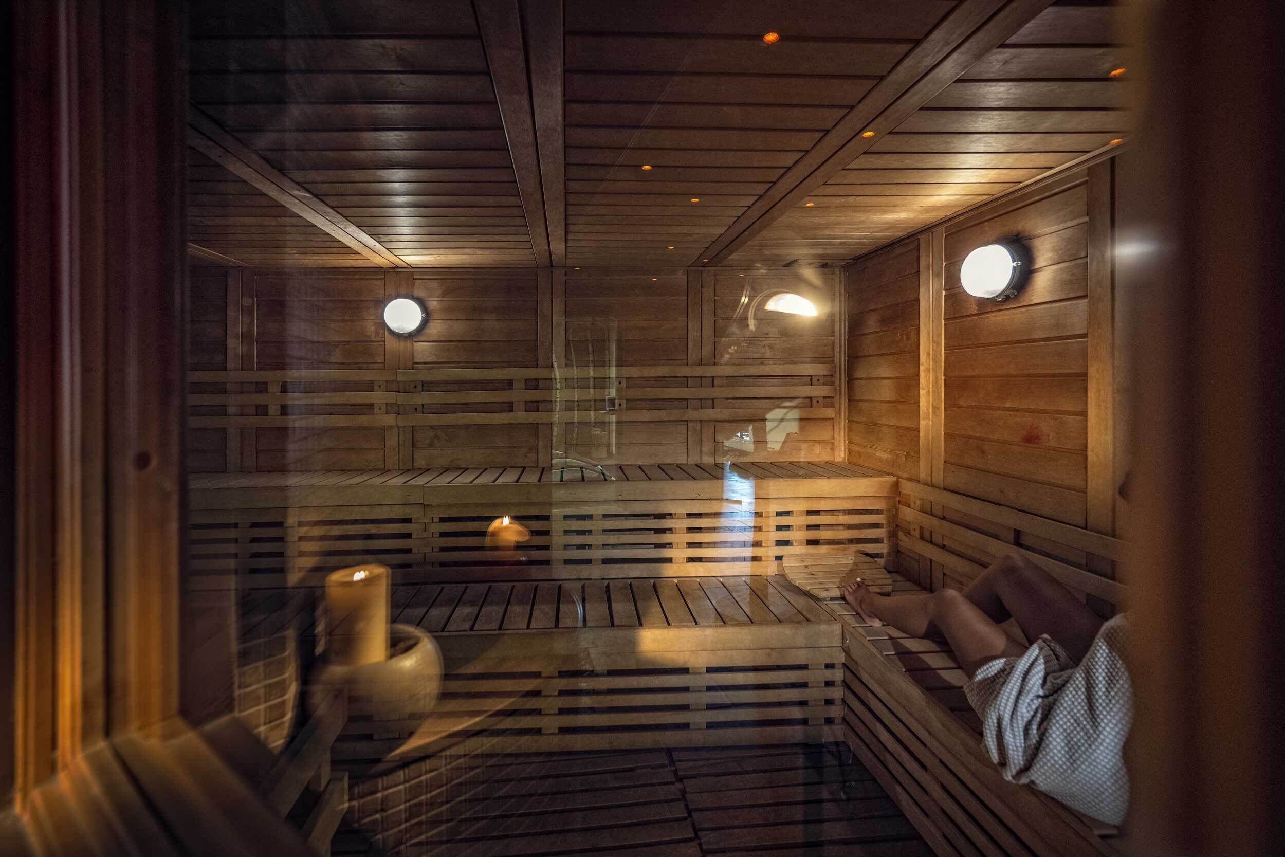 A sauna with wooden walls and benches, a glass door, and a candle on the floor.