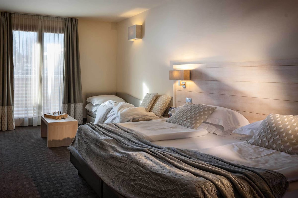 A hotel room with a large bed, a bedside table, a lamp, and a view of the city through the window.