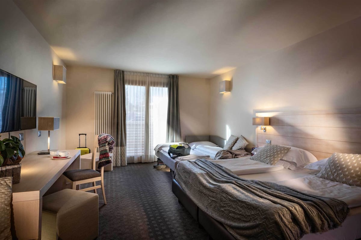 A hotel room with a bed, a desk, a chair, a TV, and a window with curtains.