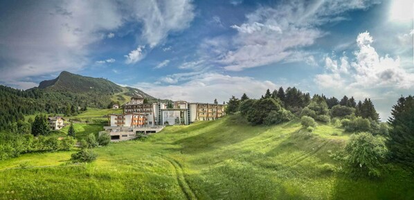A hotel with multiple buildings, surrounded by lush green hills and a mountain in the background.