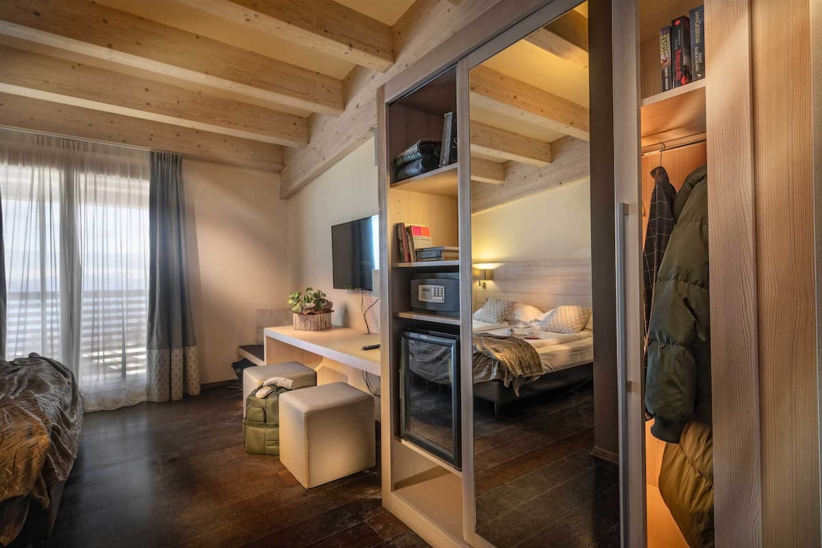 A modern bedroom with a wooden ceiling, a bed with a white headboard, a desk with a computer, a bookshelf, and a coat rack.