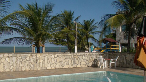 A pool area with stone walls, white plastic chairs, and palm trees. - Beach Hotel Jacumã (Conde)