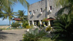 A building with a stone facade, outdoor seating, palm trees, and a playground. - Beach Hotel Jacumã (Conde)
