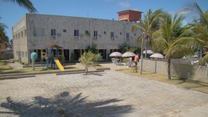 A building with a stone facade, a playground with a slide, and outdoor seating with umbrellas. - Beach Hotel Jacumã (Conde)