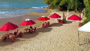 A beach with red umbrellas and tables, a sandy shore, and a clear blue sky. - Beach Hotel Jacumã (Conde)