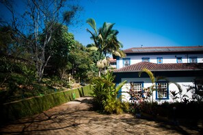 A pathway leading to a white building with blue trim and a tiled roof, surrounded by lush greenery and palm trees.