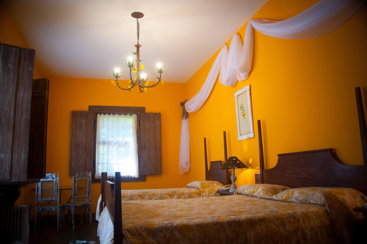 A room with two beds, a chandelier, a window with curtains, and a wooden headboard.