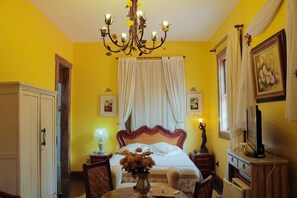 A room with a bed, a chandelier, a television, and a painting on the wall.