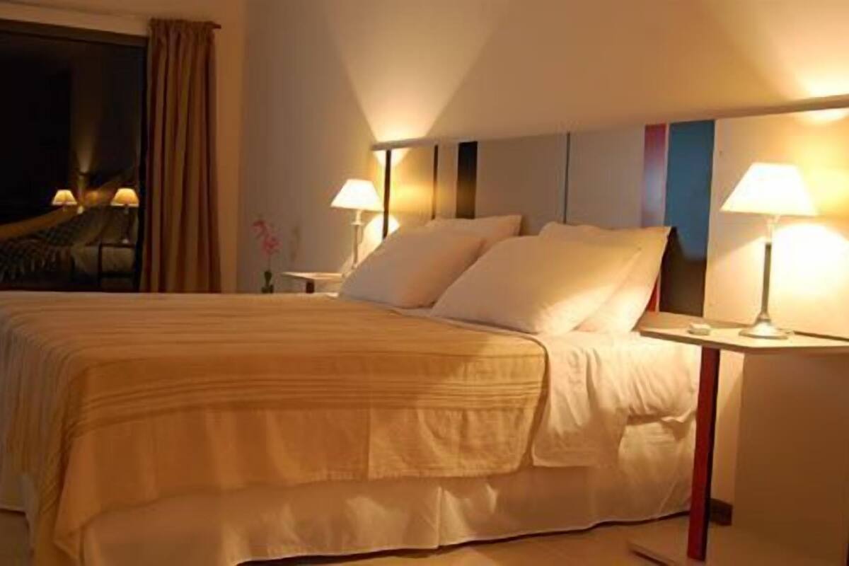 Una camera d'albergo con un letto grande, due comodini con lampade, una finestra con tende e vista sul cielo notturno.