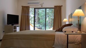 Una habitación de hotel con cama, televisión, ventana con cortinas y lámpara.