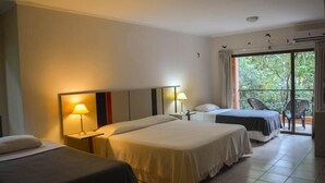 Habitación de hotel con dos camas, un balcón con sillas y vistas a la vegetación.