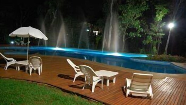 Un área de piscina nocturna con sillones reclinables y una terraza de madera.