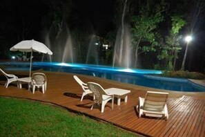 Ein Poolbereich bei Nacht mit Liegestühlen und einer Holzterrasse.