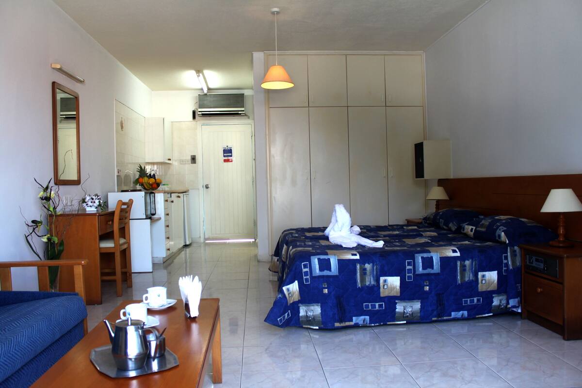 Ein Hotelzimmer mit einem Bett, einem Schreibtisch, einem Stuhl, einem Tisch mit Wasserkocher und Tassen, einer Lampe und einem Kleiderschrank.