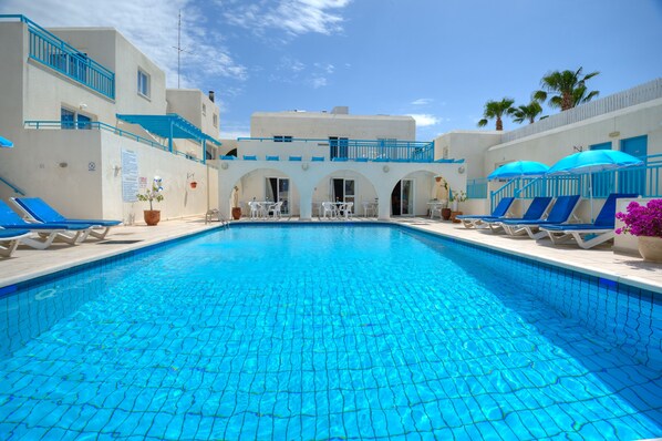 Una piscina con piastrelle blu, lettini e ombrelloni.
