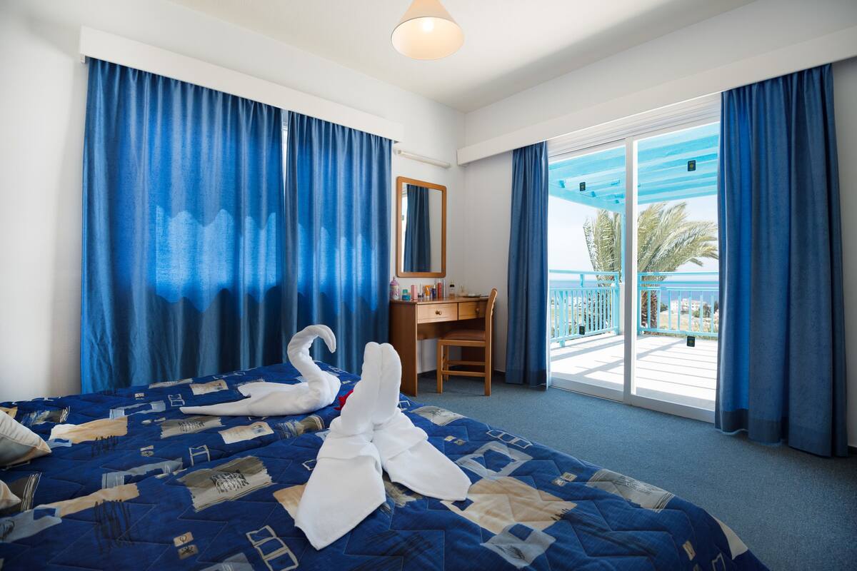 Ein Hotelzimmer mit Bett, Schreibtisch, Stuhl, einem Balkon mit Blick und einem großen Fenster.