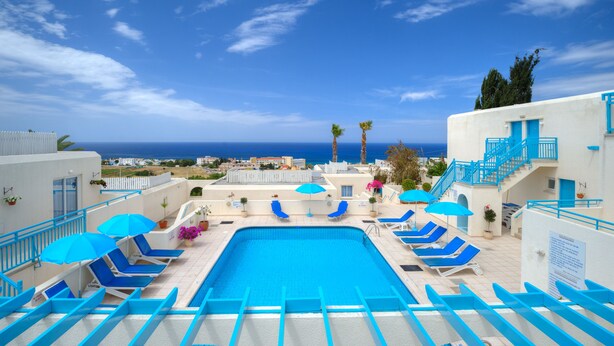 A pool area with blue chairs and umbrellas, a staircase, and a view of the sea. - Sunny Hill Hotel Apartments (Chlorakas)