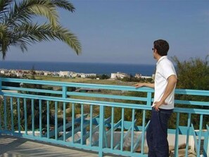 Un uomo in piedi su un balcone con vista sul mare e sugli edifici in lontananza.