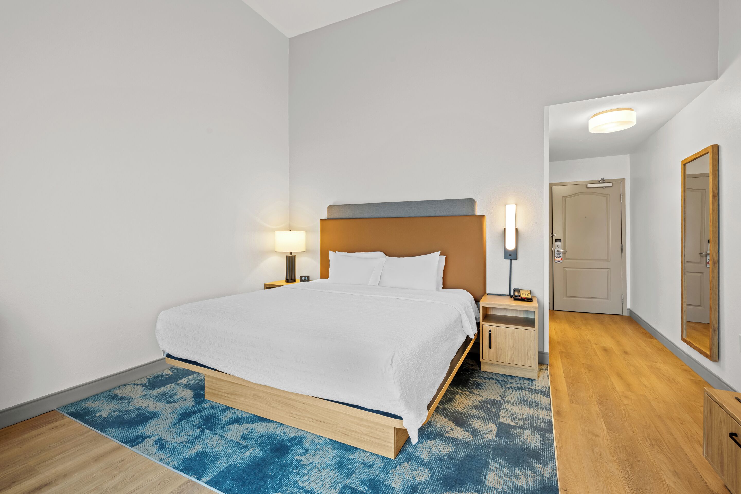 A hotel room with a bed, bedside tables, a lamp, a mirror, and a door.