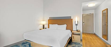 A hotel room with a bed, bedside tables, a lamp, a mirror, and a door.