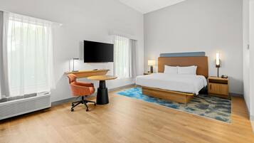 Quarto de hotel com cama, escrivaninha, cadeira, televisão e janela.