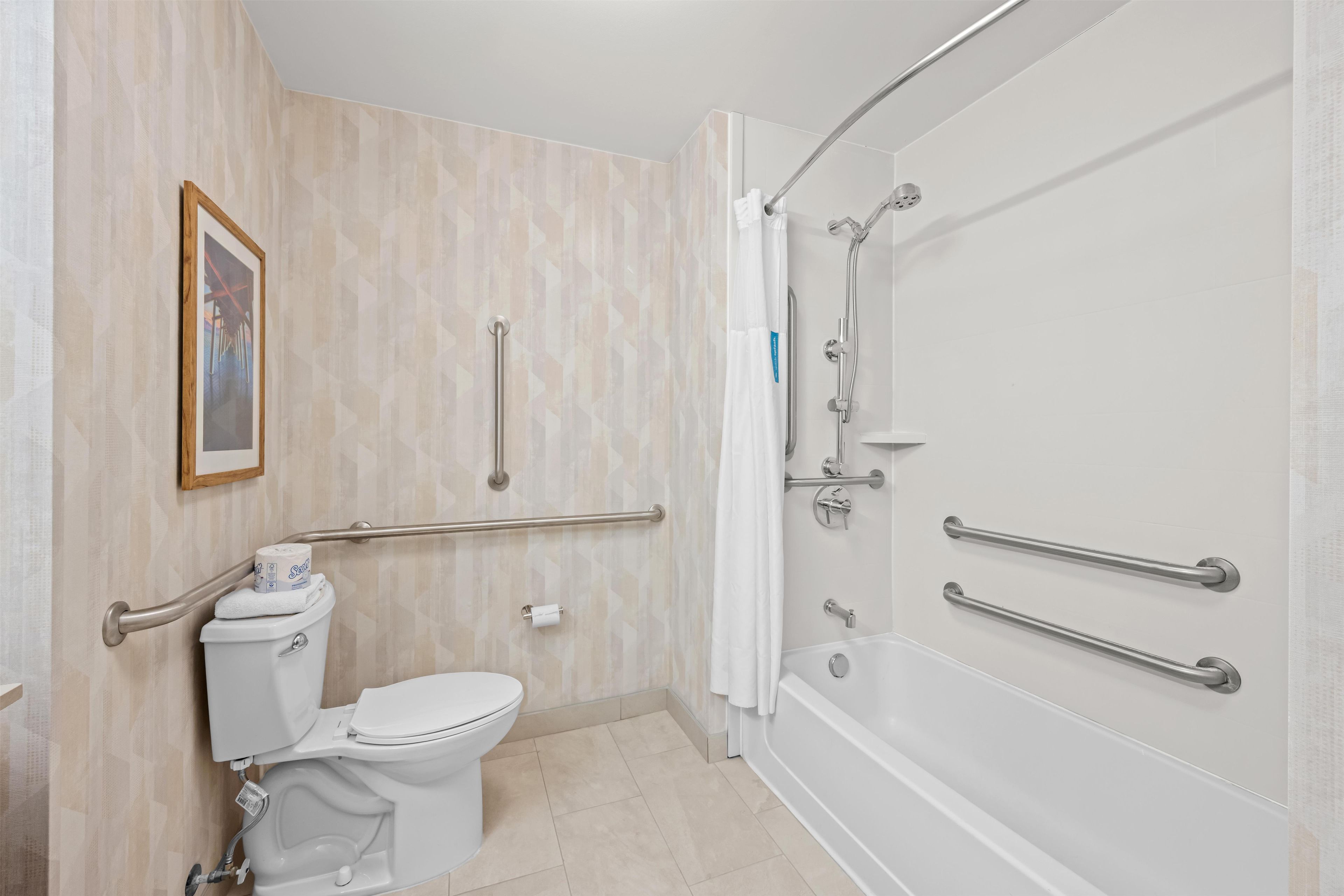 Baño con inodoro, bidé y bañera, equipado con barras de apoyo y asiento para ducha.