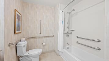 Baño con inodoro, bidé y bañera, equipado con barras de apoyo y asiento para ducha.