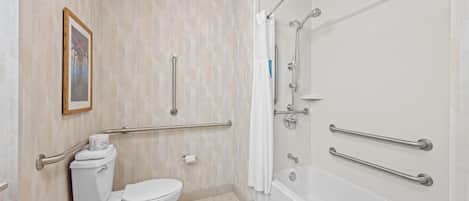 A bathroom with a toilet, bidet, and bathtub, equipped with grab bars and a shower chair.