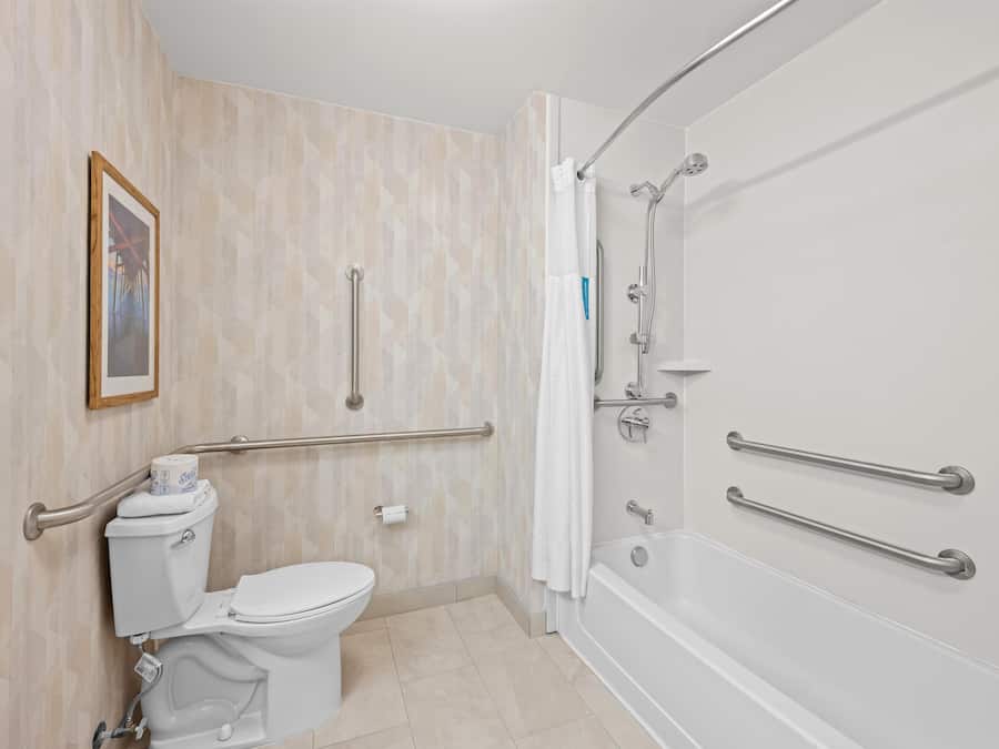 A bathroom with a toilet, bidet, and bathtub, equipped with grab bars and a shower chair.