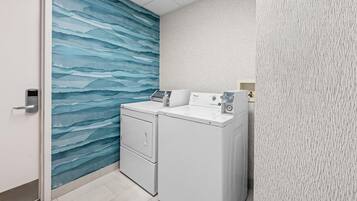 Un lavadero con lavadora y secadora Whirlpool, una puerta con cerradura de tarjeta de acceso y una pared con diseño de olas azules.