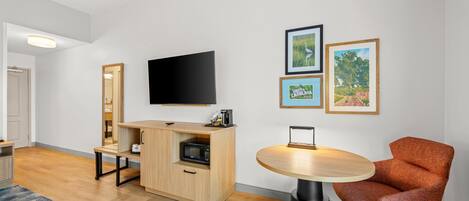 Una sala de estar moderna con televisor de pantalla plana, un mueble de madera, una mesa redonda con una silla y cuadros enmarcados en la pared.