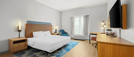 Habitación de hotel con cama, mesitas de noche, escritorio, silla, televisor y ventana con cortinas.