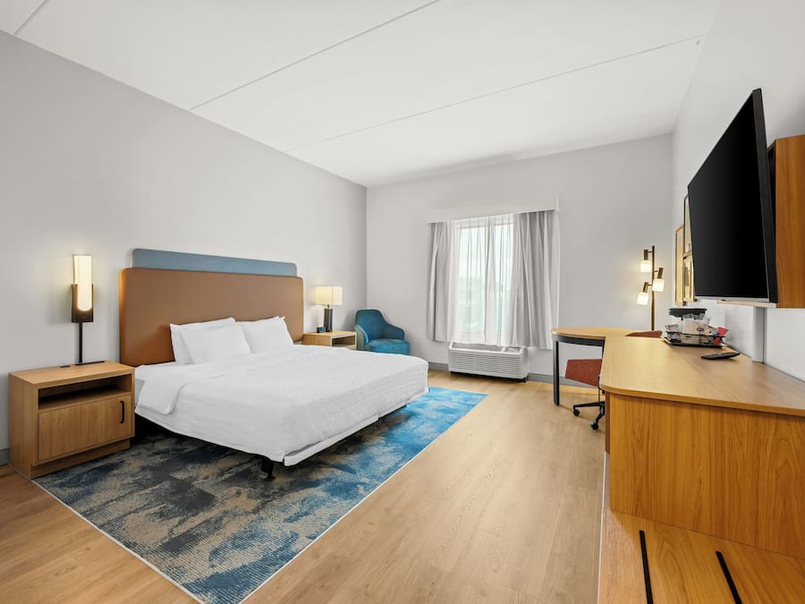 A hotel room with a bed, bedside tables, a desk, a chair, a TV, and a window with curtains.