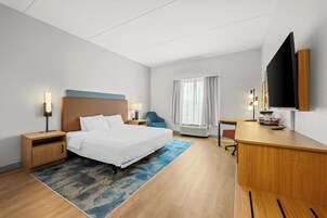 Habitación de hotel con cama, mesitas de noche, escritorio, silla, televisor y ventana con cortinas.