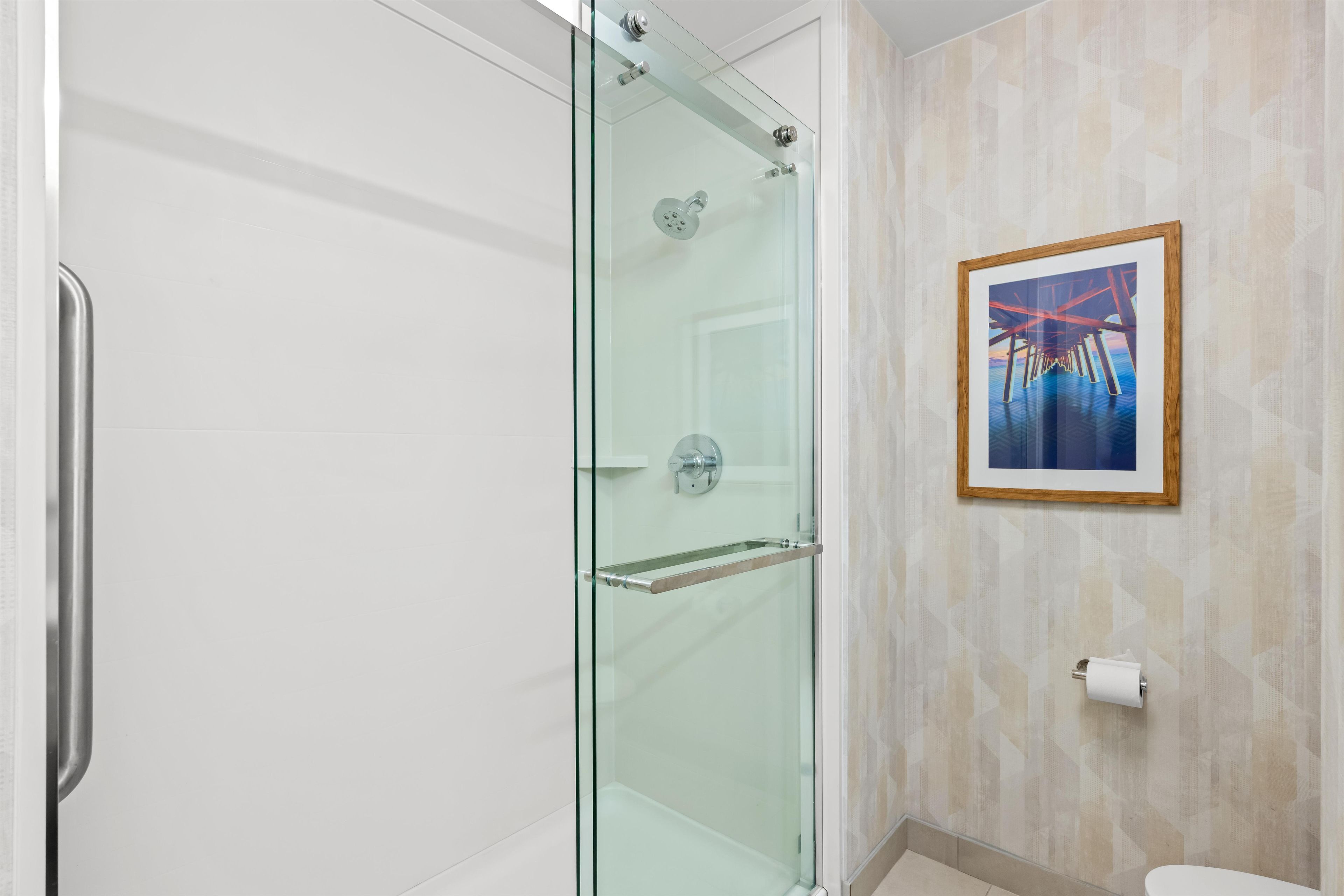 A modern bathroom with a glass-enclosed shower, a framed artwork on the wall, and a toilet paper holder.