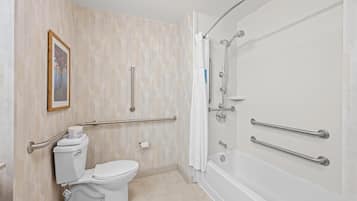 A bathroom with a toilet, bidet, and bathtub, equipped with grab bars and a shower chair.
