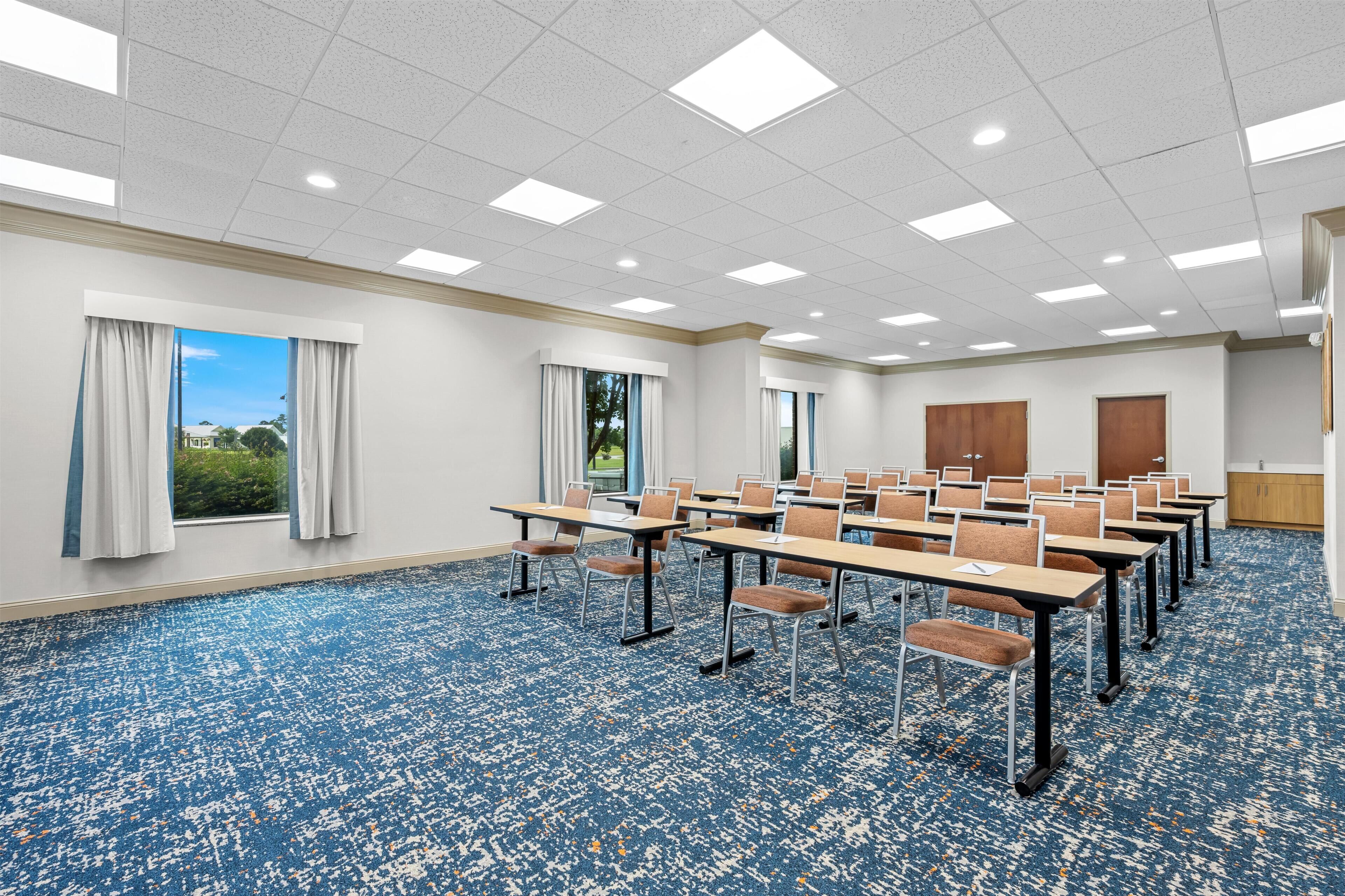 A conference room with a blue carpet, white walls, and a large window with curtains.