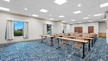 A conference room with a blue carpet, white walls, and a large window with curtains.