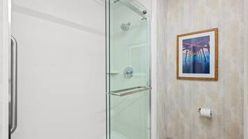 A modern bathroom with a glass-enclosed shower, a framed artwork on the wall, and a toilet paper holder.