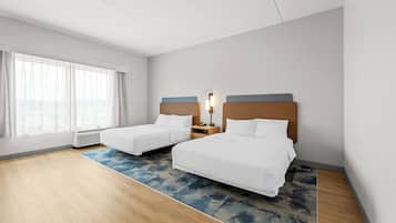 Een hotelkamer met twee bedden, een groot raam met gordijnen, een elektrische kachel en een blauw tapijt met een patroon.
