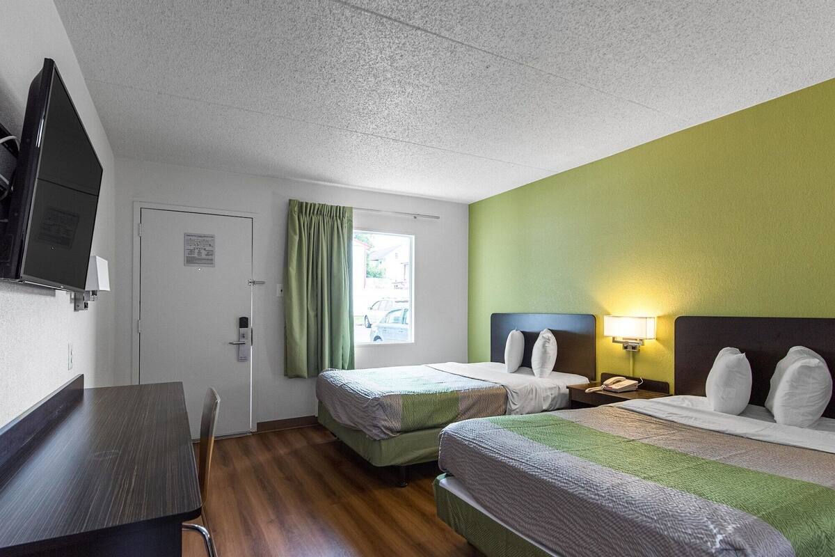A hotel room with two beds, a desk, a TV, and a window with curtains.