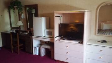 A compact hotel room with a kitchenette, a television, a desk, and a bed.