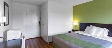 Una habitación de hotel con cama, escritorio, silla, lámpara y puerta.